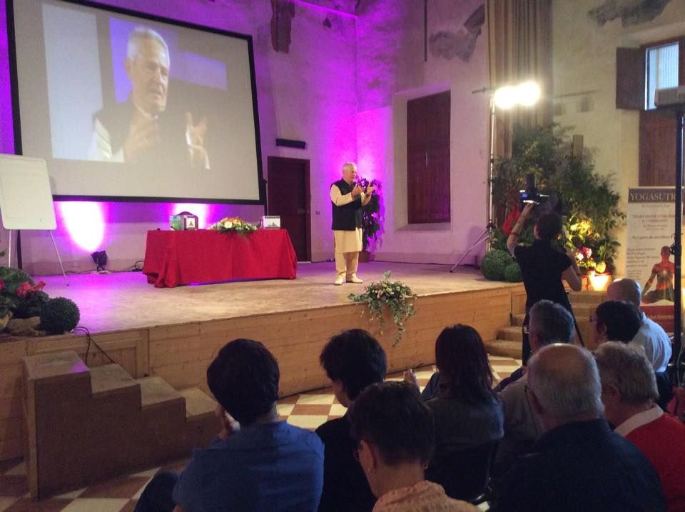 Marco Ferrini su un palco con maxi schermo alle spalle e pubblico davanti, in una sala storica di Ferrara